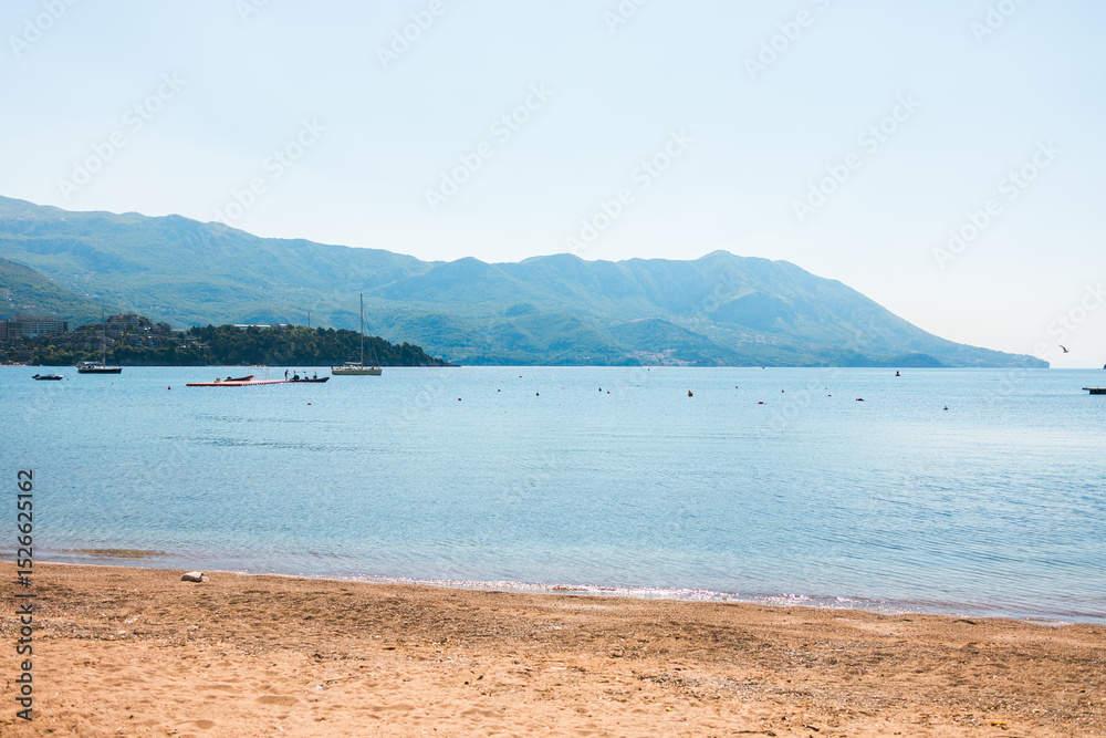 Fototapeta premium Tranquil beach with calm sea and mountain background. Coastal serenity, nature landscape, and summer relaxation destination.