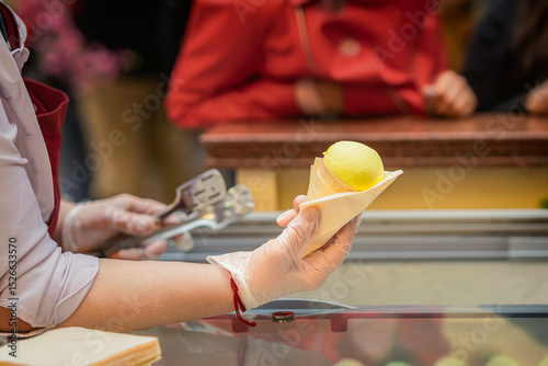 Close-up of vendor holding yellow ice cream cone over counter in public place. Concept of ice cream, frozen product in summer, sweet craving, refreshment. Small business support