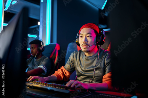 Focused male gamer competing in esports tournament with headsets and neon lighting