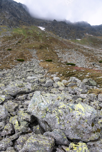 Alpine wilderness scenery featuring dark misty mountain slopes, rocky terrain under cloudy sky