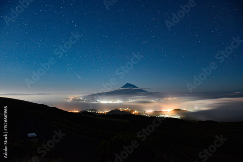 Stunning Night Sky Over Mountainous Landscape over Azores with City Lights at night 