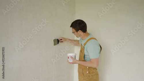 Professional house painter mixes and applies putty with a spatula, smoothing wall surface for painting, preparing walls for final finishing