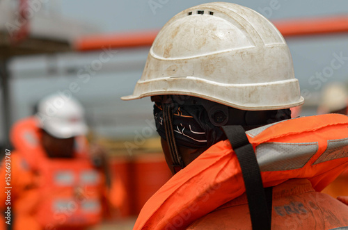 An old and dirty safety helmet sits on a seafarer head during the emergency drill on board of the offshore support vessel. Helmet is essential piece of basic personal protective equipment photo