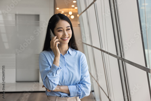Chinese businesswoman engaged in formal conversation with client on mobile phone, smiling, discussing project details, scheduling meeting, providing feedback or professional assistance by phone call