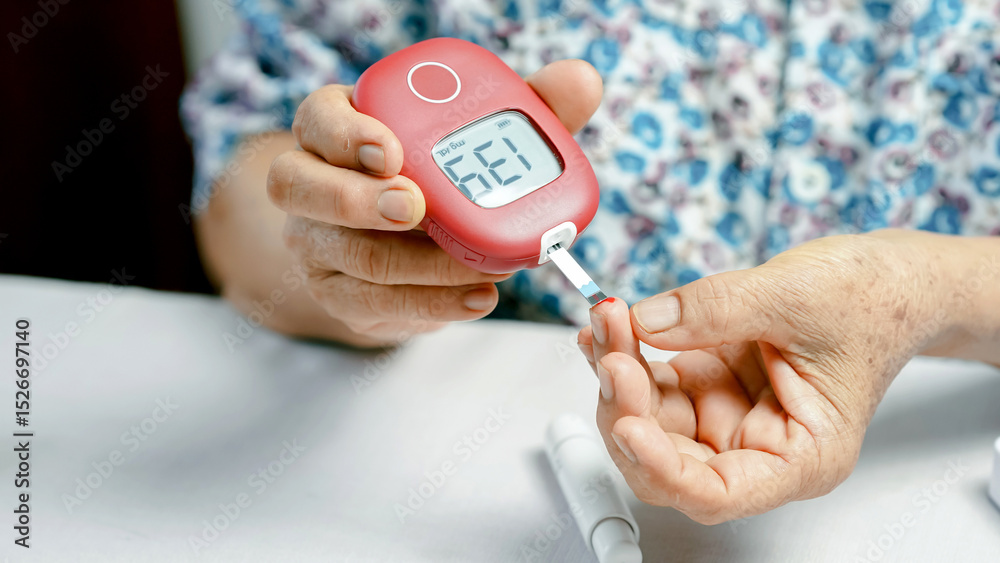 Fototapeta premium Elderly person checking blood sugar level with digital glucose meter, close up of hands, diabetes management, healthcare and medical concept, home monitoring, floral shirt visible