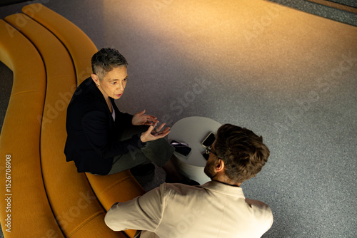 Bild auf Leinwand Two businesspeople engaging in discussion while seated on a stylish yellow sofa