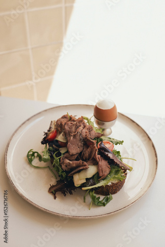 Sandwich with meat, egg and with freshly greens. Crop delicious breakfast served on wooden table in sunny cafe. Part of a series