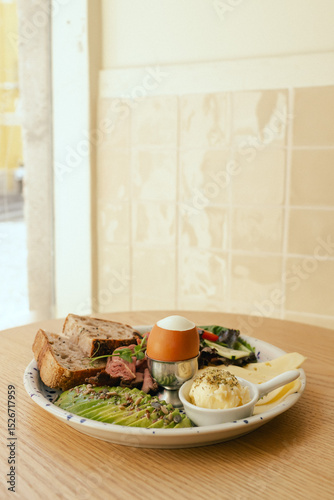 Sandwich with meat, avocado, egg and with freshly greens. Crop delicious breakfast served on wooden table in sunny indoor cafe. Part of a series