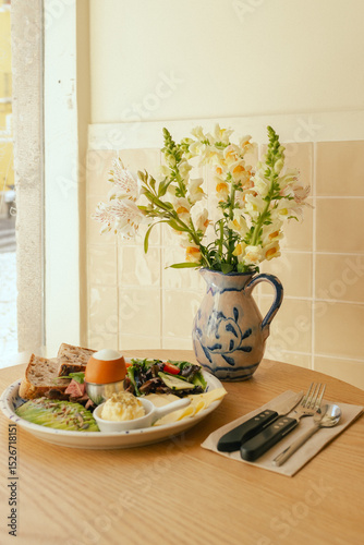 Sandwich with meat, avocado, egg and with freshly greens. Crop delicious breakfast served on wooden table in sunny indoor cafe. Part of a series