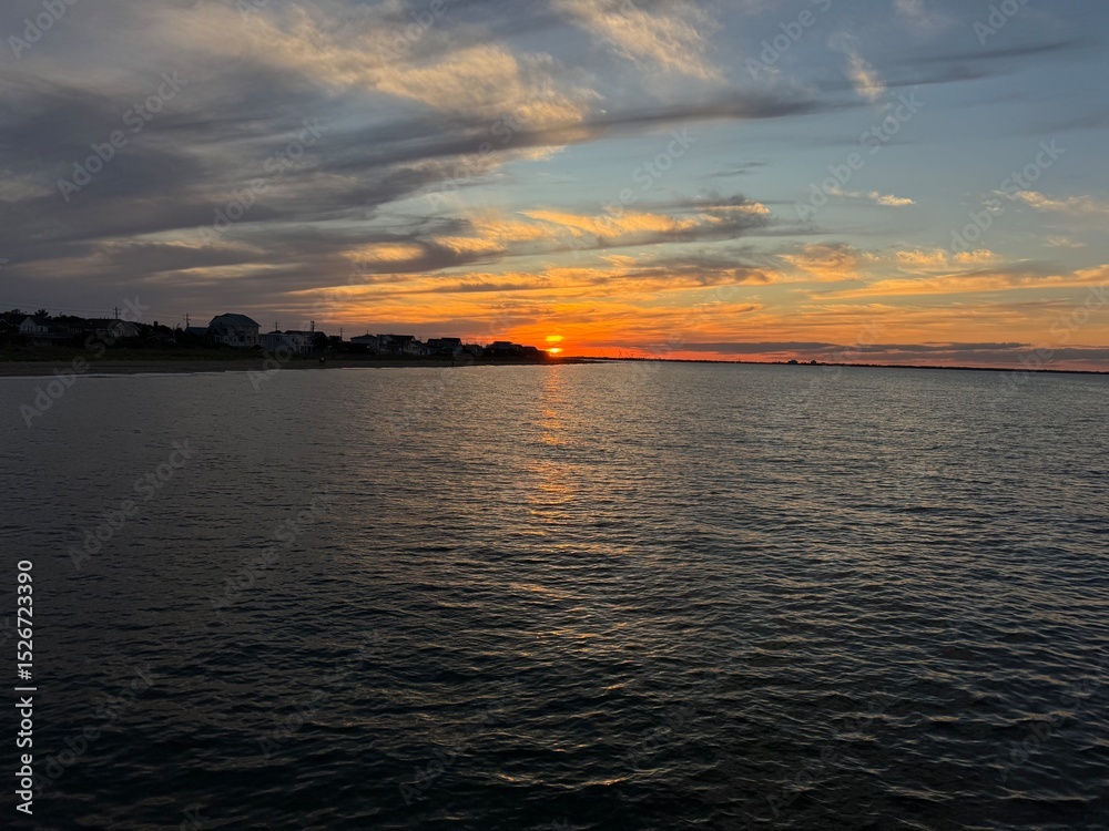 Fototapeta premium Sunset over calm ocean waters in the Ocean View area of Norfolk, Virginia with shoreline homes and a golden sky