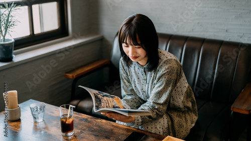 カフェのソファに座って雑誌を読む若い女性
