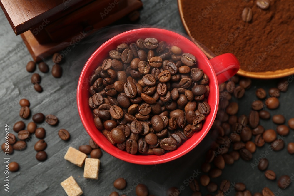 Fototapeta premium Aromatic coffee beans in cup, grinder and brown sugar on black table, flat lay