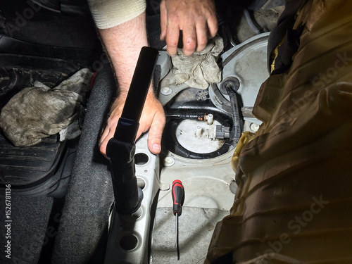 Mechanic checking automotive fuel system under rear seat, diagnostic tools and hands visible, professional car repair service and maintenance.