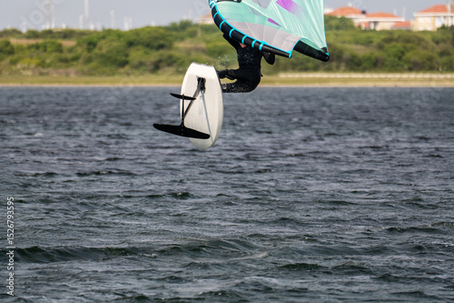 Close-up from a man in a black wet suit jumping with a wing foil at sunny weather in Netherland.