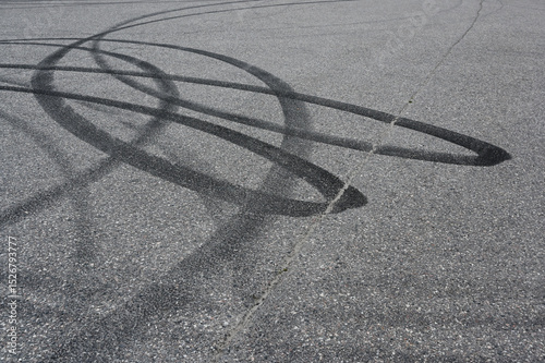 an asphalt surface covered in overlapping tire skid marks from high-speed driving maneuvers such as drifting or burnouts