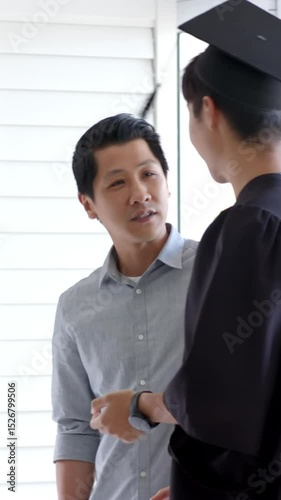 Vertical video: Asian father and son greeting at foyer while handing gown and adjusting mortarboard