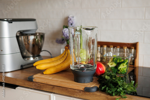 Healthy ingredients for detox smoothie drink and lifestyle diet. Glass blender bowl, apple, banana, broccoli, parsley on table top at modern home kitchen. Fresh fruits, vegetables and greens