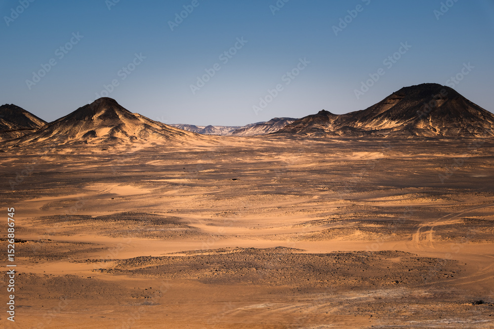 Naklejka premium Ash-covered hills in Egypt's Black Desert under a clear sky, scenic and remote landscape. Volcanic