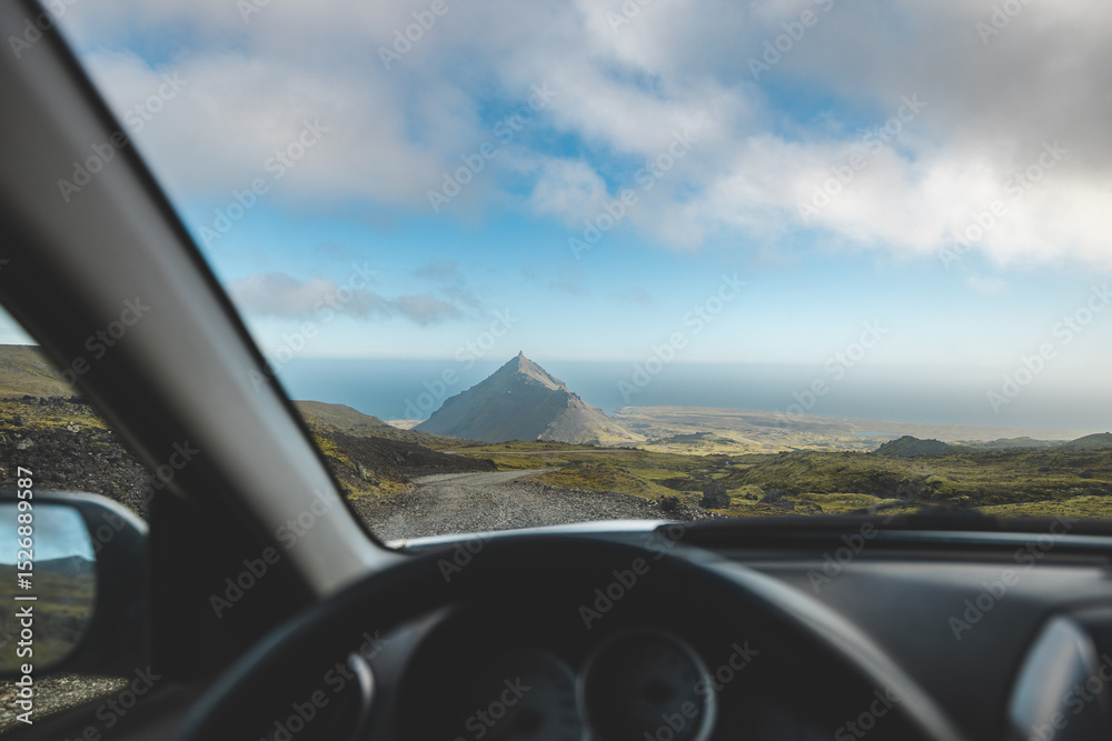 Naklejka premium Driving along a rugged gravel road toward a striking mountain peak on Iceland Snaefellsnes Peninsula. A perfect moment of road trip freedom and adventure