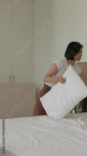 Vertical video: After unpacking boxes diverse couple pulling pillows, shaking duvet on bed at home