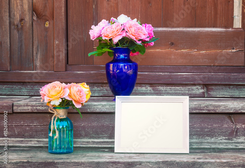White frame and bouquets of roses in vases are on steps of rustic wooden ladder.