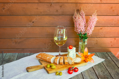 Glass of wine, blue cheese, baguette, cherry tomatoes, olives, lily and astilbe flowers.