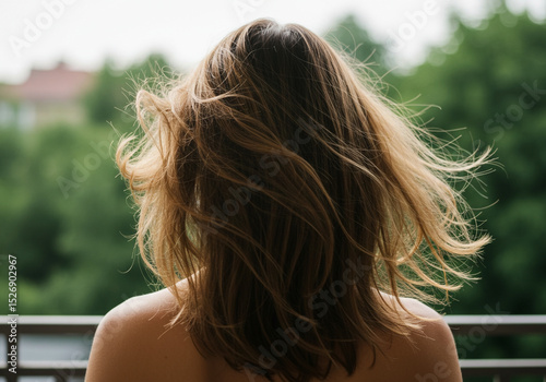 Woman with windblown brown hair looks out at a lush green landscape, enjoying nature's tranquility.