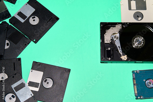 A collection of floppy disks and hard drives, relics of different technological eras, contrast against a turquoise background