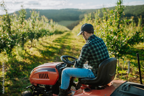 Farmer mowing between fruit trees in his orchard.