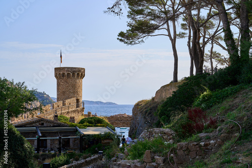 The scenic coastal views of Tossa de Mar, showcasing a medieval fortress, lush greenery, and the azure sea on a sunny day.