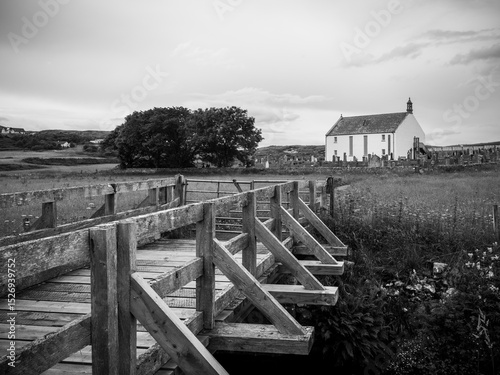 Monochrome image of wooden bridge leading towards a white church in the far distance