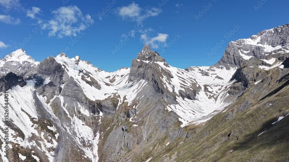 Paysage alpin spectaculaire sous un ciel bleu éclatant. D’imposants sommets rocheux et enneigés se dressent au cœur des montagnes, offrant une vue majestueuse et sauvage. Vidéo drone 4k 60fps