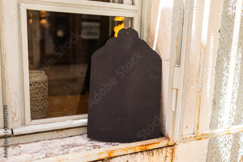 Fototapeta Naklejka Na Ścianę i Meble -  Blank chalkboard sign on windowsill in rustic setting. Outdoor signage, vintage decor, and small business ambiance in a Mediterranean street