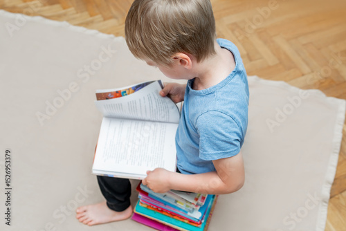 Little boy kid child sitting on stack of children's books and leafing through a book with pictures of fairy tales,learning read.Education