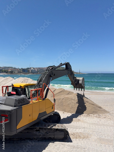 Excavator moving sand on the beach on a sunny day with blue sky and ocean
