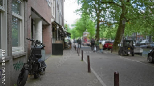 Wallpaper Mural Street scene in amsterdam with blurred people walking, bicycles, and trees lining a canal in a lively urban setting. Torontodigital.ca