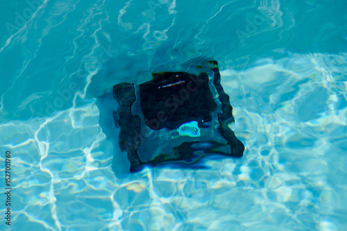 Robotic pool cleaner operates in clear blue water during sunny afternoon by the backyard pool