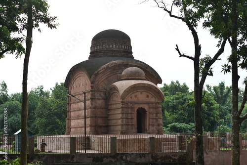 Ancient Bhubaneswari Temple stands amidst green trees under a cloudy sky.