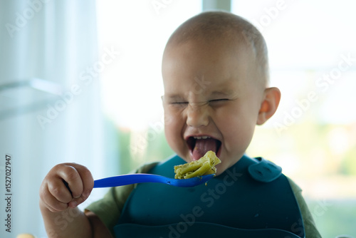 Beaming toddler successfully using spoon to eat broccoli, radiating happiness and food enjoyment. Positive weaning experience with healthy vegetables.