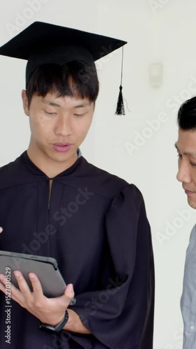 Vertical video: Asian father and son tapping tablet opening graduation gift box at home, copy space