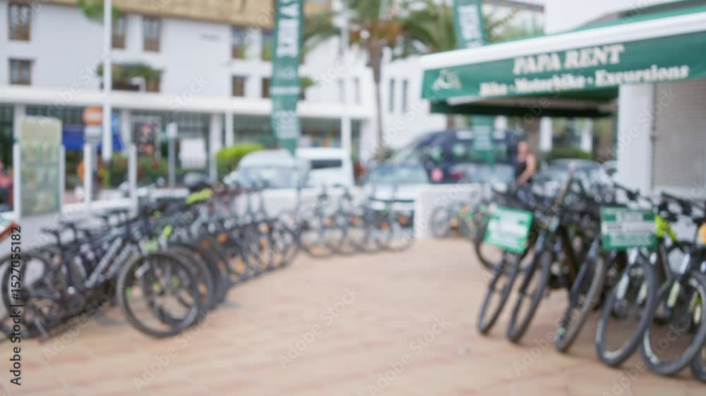 Rental bikes lined up under a bokeh background with blurred buildings and a defocused man walking in an urban area