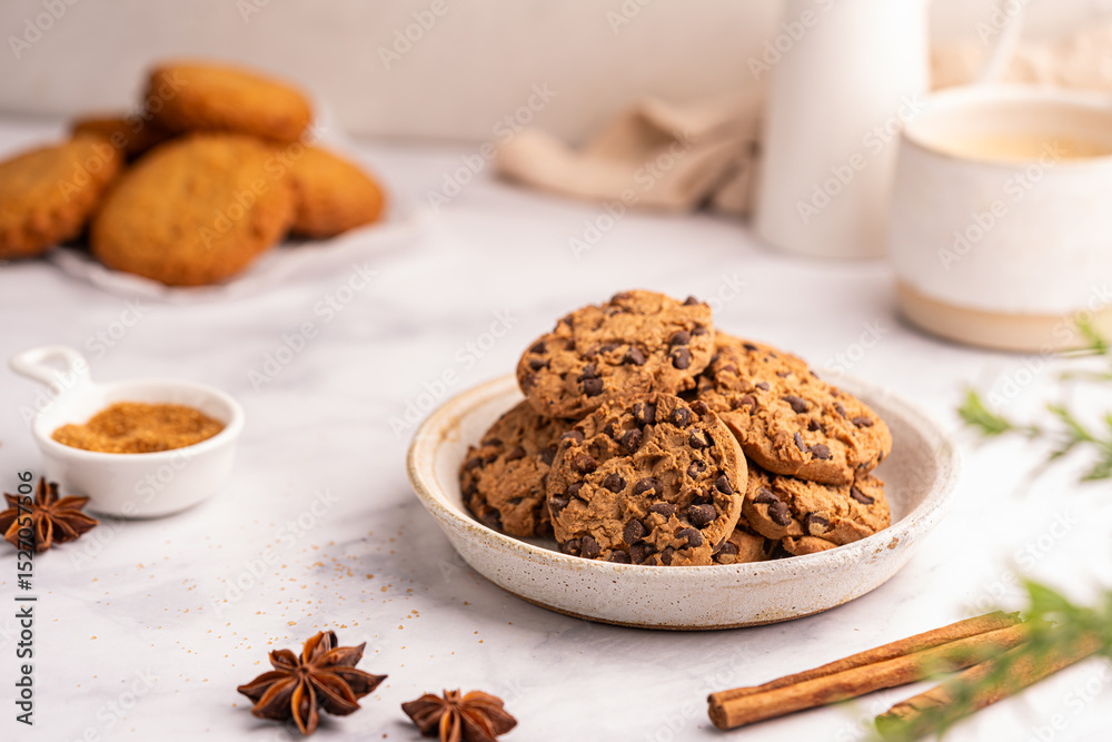 Fototapeta premium Golden chocolate chip cookies next to a glass of milk on white kitchen background. High quality photo