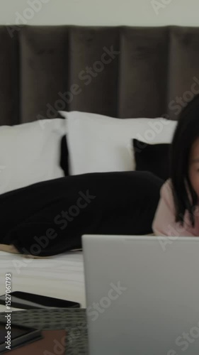 Vertical video: Asian woman viewing laptop, typing passport, card info booking flight in bedroom