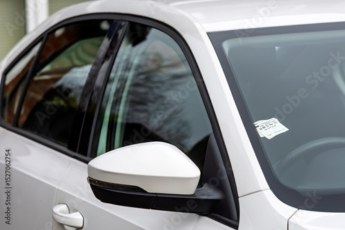 A pay-and-display parking ticket is displayed on the dashboard of a modern white car. The image represents city parking, transportation costs, following rules, and urban life