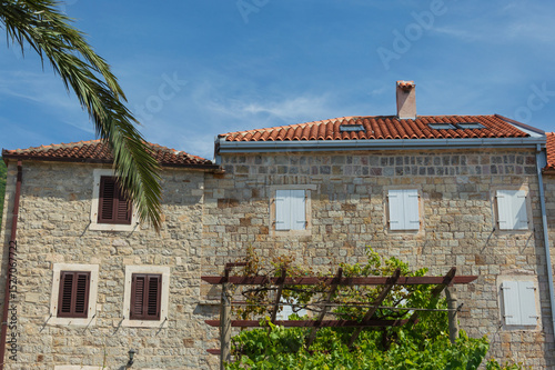 Fototapeta Naklejka Na Ścianę i Meble -  Old stone house with small windows, tiled roof and blue sky on the Adriatic coast in Montenegro Petrovac