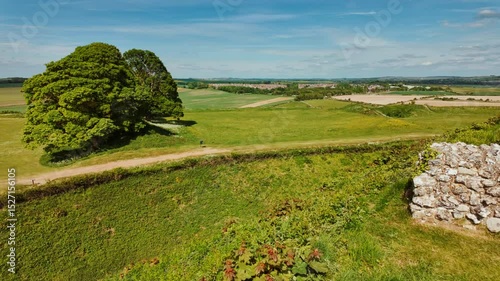 Overgrown grass carpets the ancient walls and ditches of Old Sarum under a wide sky, Salisbury, Wiltshire, England, UK