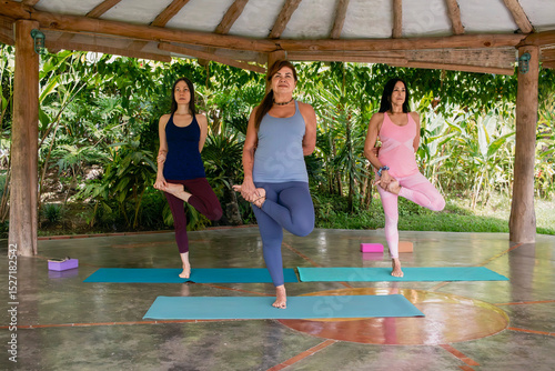 Three diverse women practicing tree pose yoga class outdoors