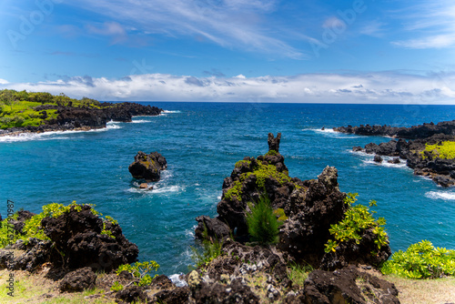 Scenic view of the Hawaiian coastline with black volcanic rocks and turquoise water under a blue sky.