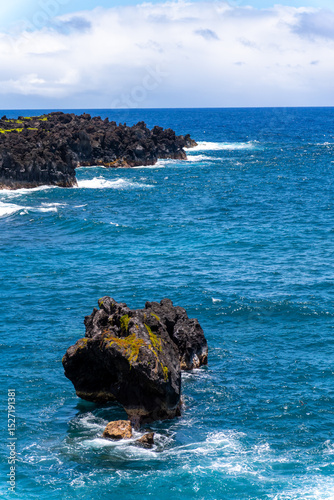Ocean view with black rocks and blue water under a cloudy sky.