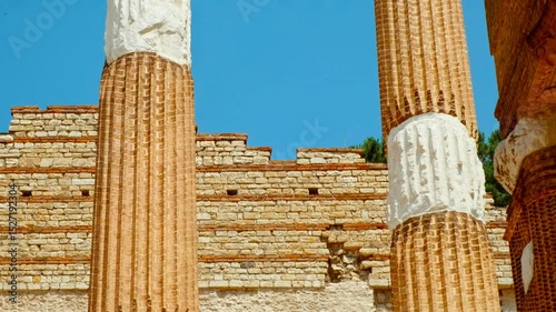 Weathered Doric columns and carved entablature fragments rising from manicured lawns in the heart of ancient Brescia, Lombardy, Italy
